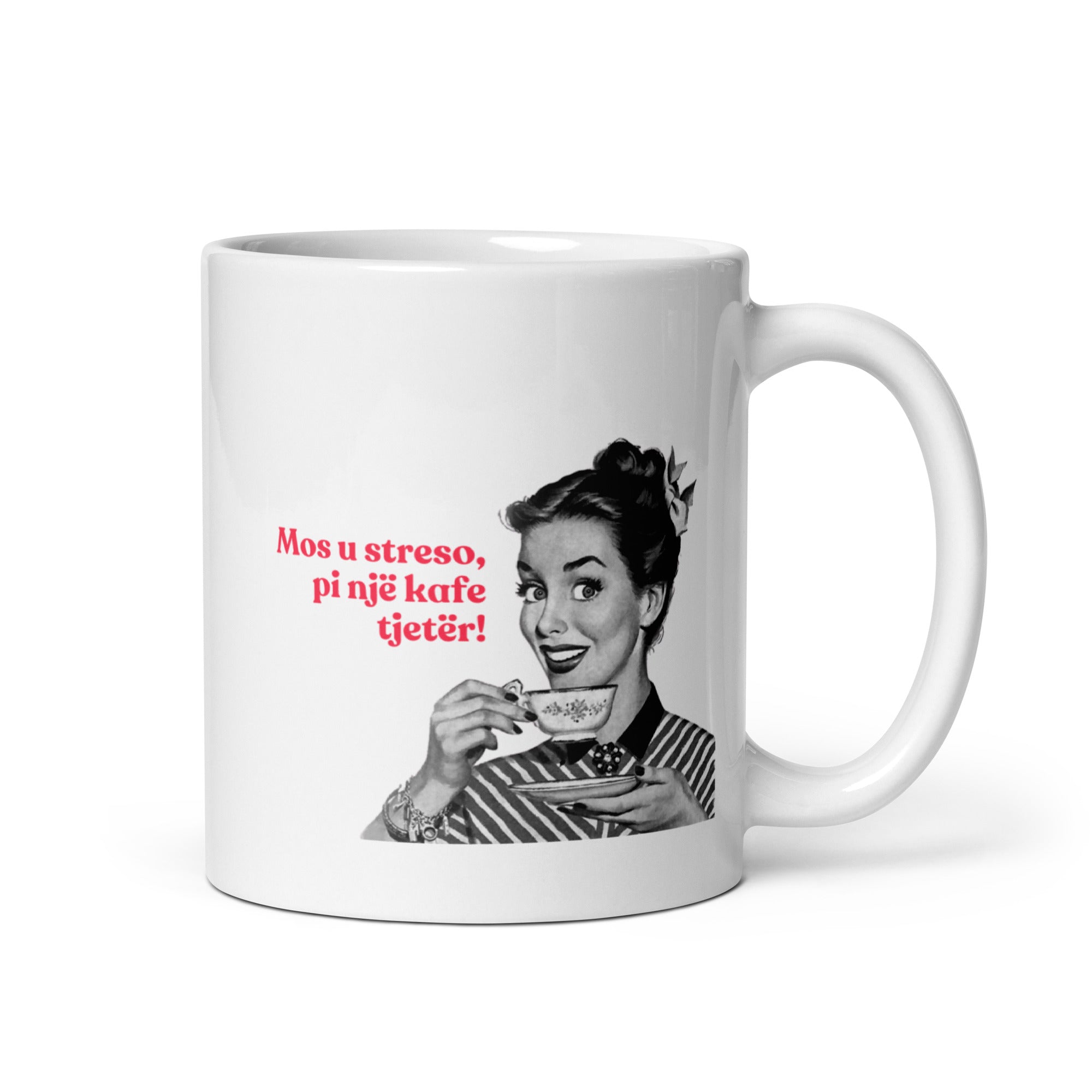 White mug with an illustration of a woman drinking coffee and the Albanian phrase “Mos u streso, pi një kafe tjetër!”