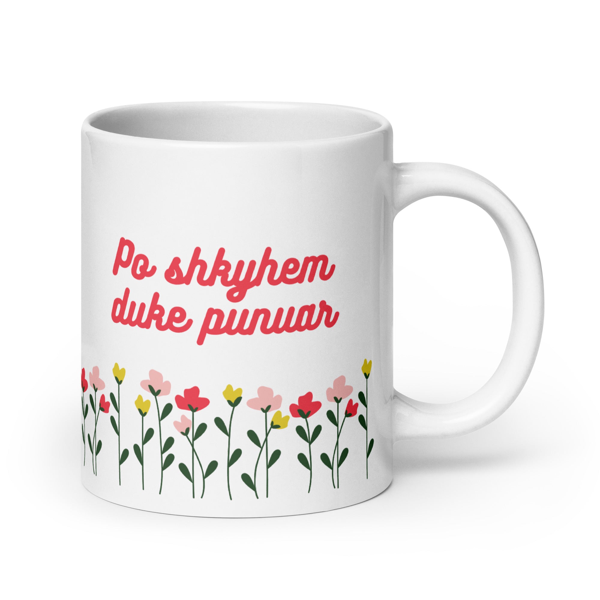 White mug with red text reading “Po shkyhem duke punuar” above colorful flowers.
