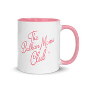 White mug with pink handle reading “The Balkan Moms Club.”
