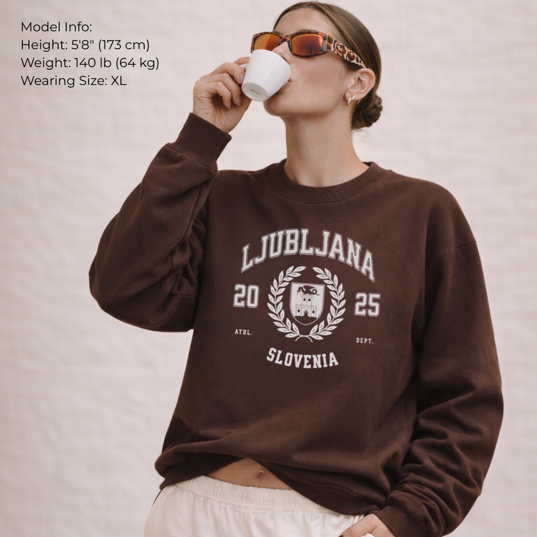 Person wearing a brown sweatshirt with 'Ljubljana 2025 Slovenia' text, drinking from a white mug.