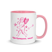 White mug with pink handle and interior featuring a cupid illustration and the Macedonian phrase “Ајде Купидоне, чекам!”
