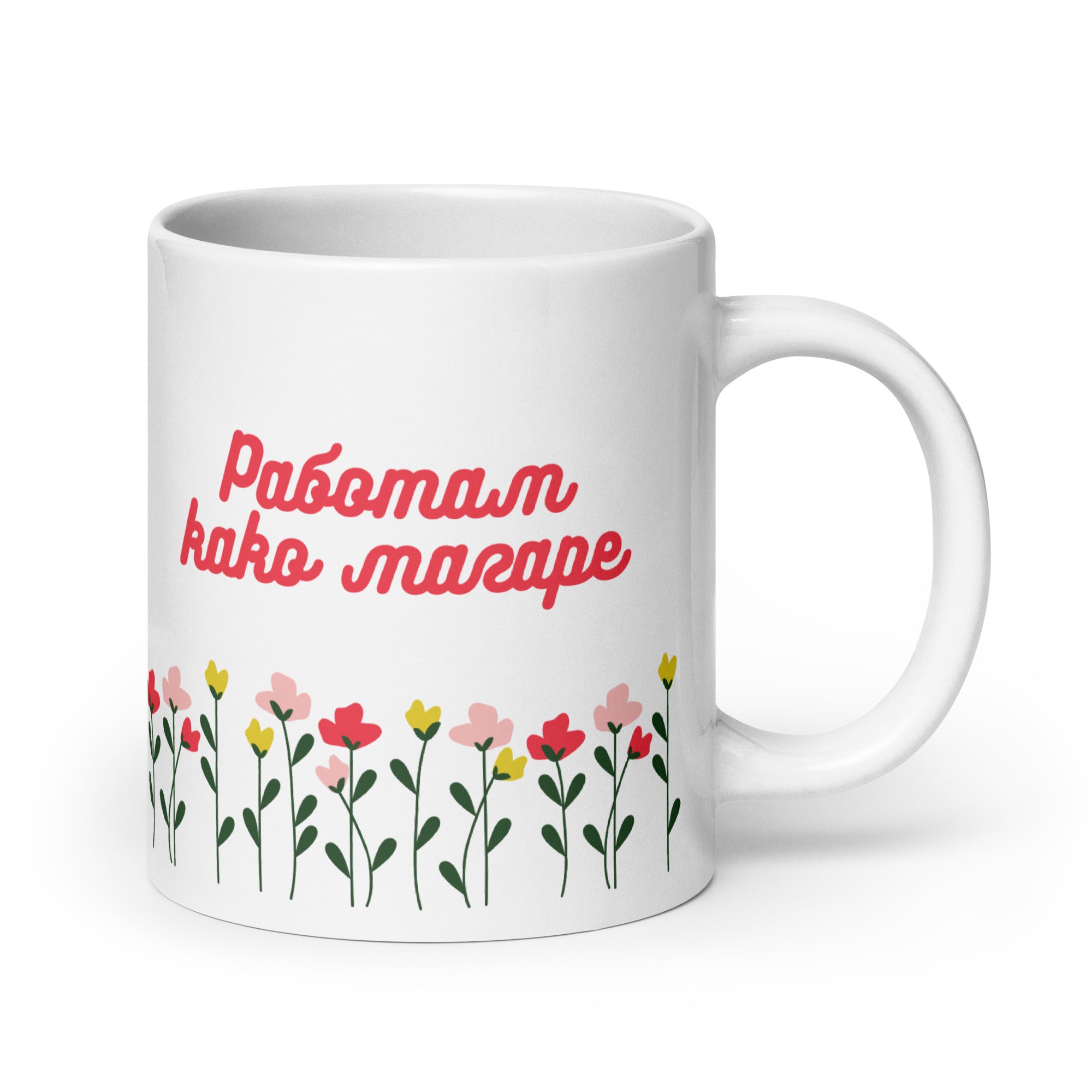 White mug with red text reading “Работам како магаре” above colorful flowers.