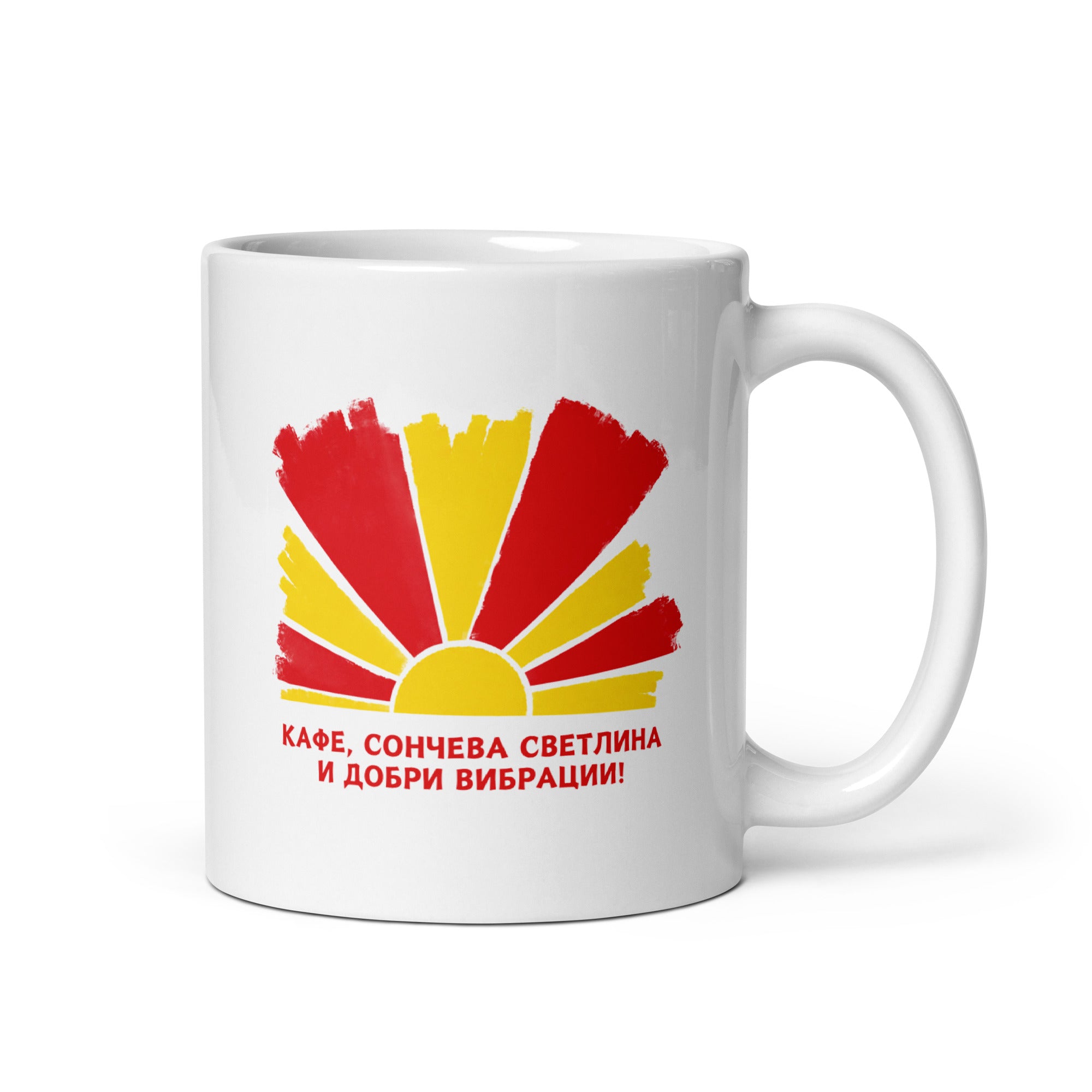 White mug with a red and yellow sunburst design and the Macedonian phrase “Кафе, сончева светлина и добри вибрации!”