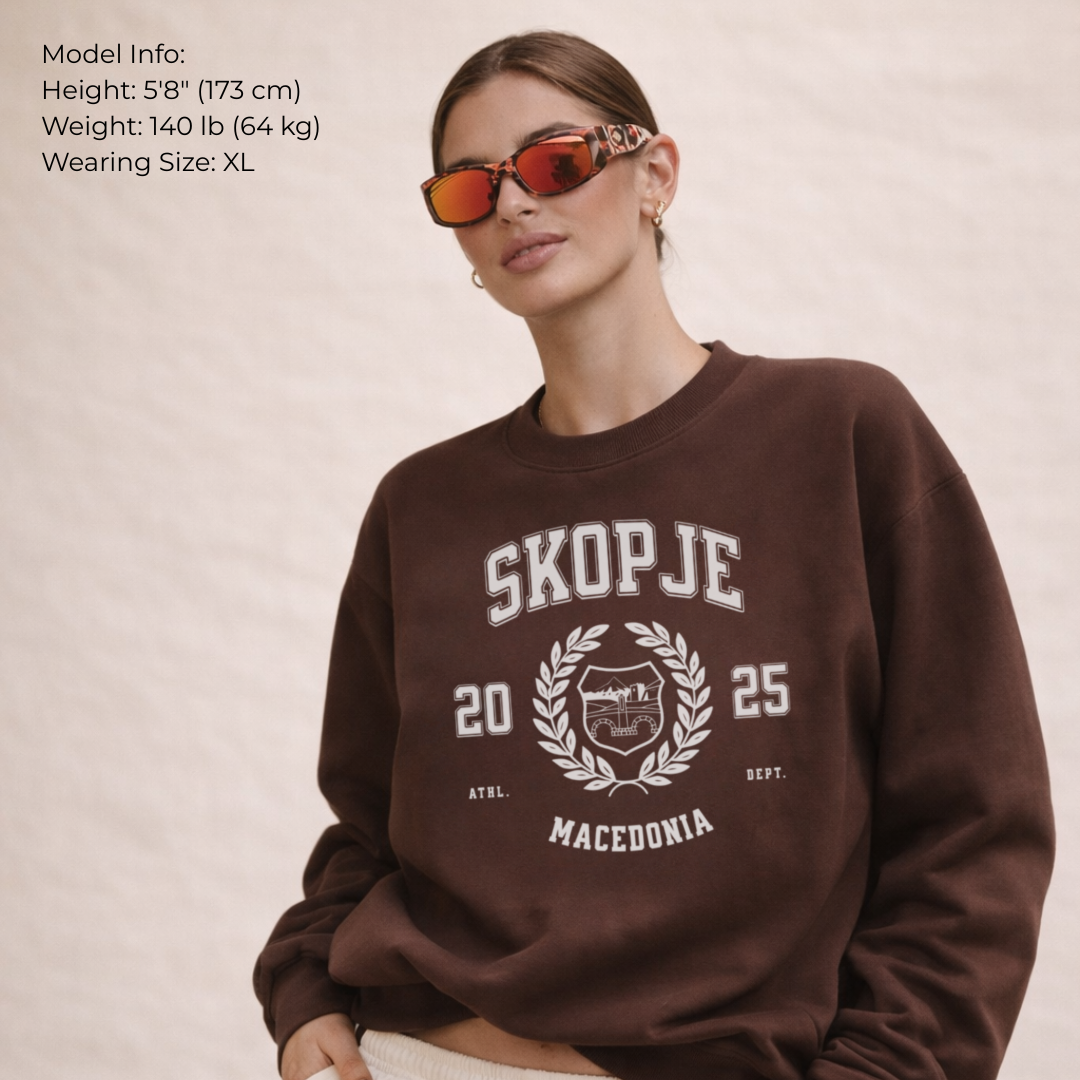 Person wearing a brown sweatshirt with 'Skopje 2025' text and design on a beige background